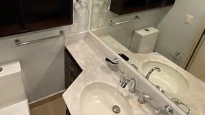 A modern bathroom with two sinks, a toilet, and a vanity with a mirror. - Condos PDS (Mazatlán)