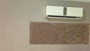 Un salon avec un canapé en cuir noir, un sol carrelé et un climatiseur fixé au mur.