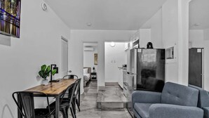 A modern kitchen with a dining area, a gray sofa, and a plant on the table.