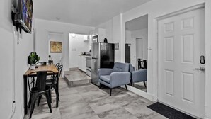 A modern kitchen with a refrigerator, microwave, and stove. There is a dining area with a table and chairs. The room has white walls and a tiled floor.