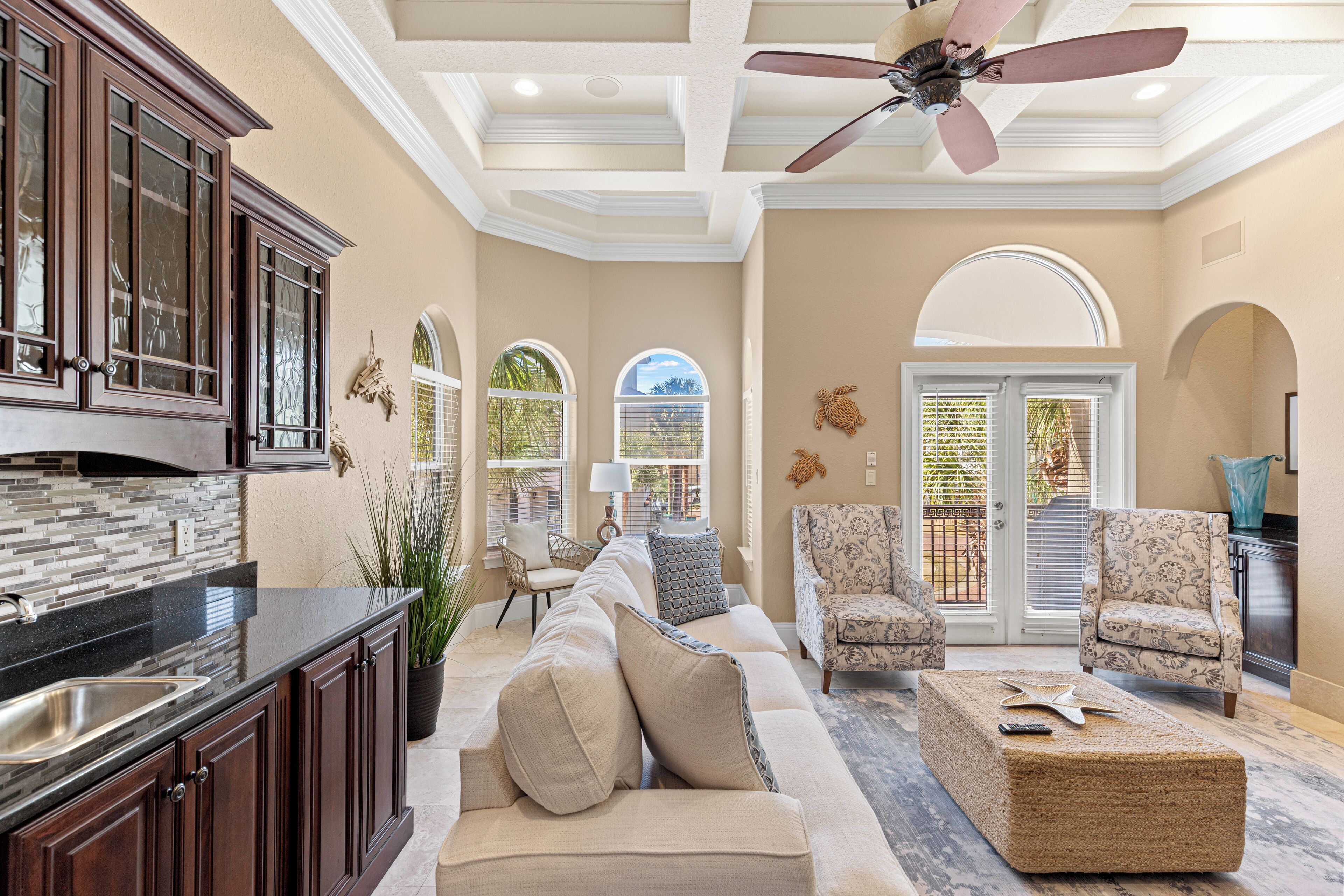 A spacious living area with a large sofa, two armchairs, a coffee table, and a kitchen with dark wooden cabinets and a black countertop.