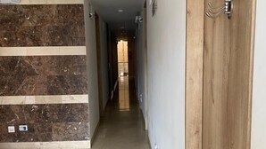 Ein Korridor mit einer Marmorwand links, einer Holztür rechts und einem gefliesten Boden.