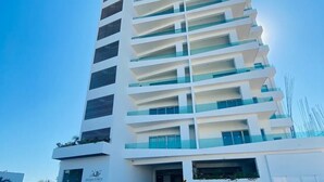 A modern high-rise building with multiple balconies, a parking garage, and a clear sky. - CASAS PB (Mazatlán)