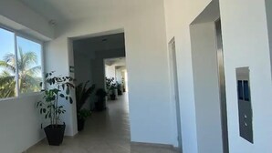 A spacious hallway with a tiled floor, potted plants, and a view of palm trees outside. - CASAS PB (Mazatlán)