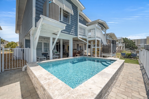 Ein Poolbereich mit klarem, blauem Pool, einer überdachten Terrasse und einem zweistöckigen Haus mit Balkon.