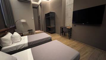 A modern hotel room with two beds, a desk, a chair, a TV, and an air conditioning unit.