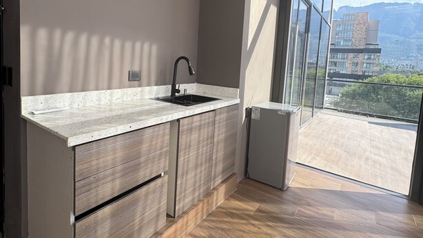 A modern kitchen with a built-in sink, wooden cabinets, and a large window overlooking a cityscape. - Amae21 Lofts (San Pedro Garza García)
