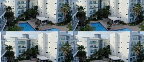 Un hotel moderno con varios balcones, una piscina y abundante vegetación.
