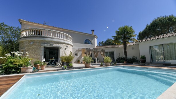 A pool area with a clear blue pool, a stone building with a balcony, and potted plants around. - Santorini bed and breakfast with terrace and swimming pool (Montreuil)