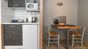 A compact kitchenette with a microwave, kettle, and small refrigerator. There is a wooden table with two chairs and a 'Cafe' sign on the wall. - Santorini bed and breakfast with terrace and swimming pool (Montreuil)