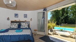A bedroom with a bed, a nightstand, a window with a view of a swimming pool and greenery. - Santorini bed and breakfast with terrace and swimming pool (Montreuil)