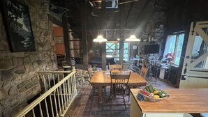 Un interior rústico con pared de piedra, mesa de comedor de madera y una zona de cocina con mostrador de madera.