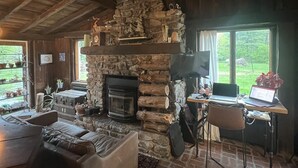 Un interior rústico con chimenea de piedra, vigas de madera, un sofá de cuero y un escritorio con una computadora portátil.