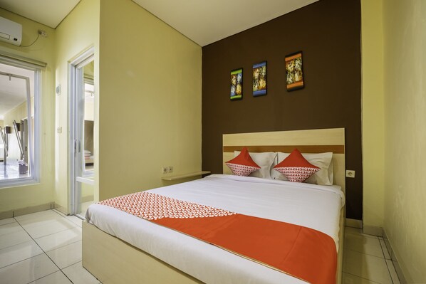 A hotel room with a large bed, a window, and a door leading to a hallway. - OYO 2947 Cluster Harris Home Stay and Kos (Cimahi)