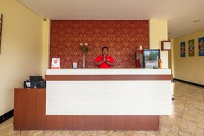 Un comptoir d’accueil aux couleurs rouge et blanc, un vase rempli de fleurs et un tableau encadré accroché au mur.