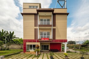 Un hôtel à plusieurs étages, doté d’une façade rouge et beige, d’un balcon au deuxième étage et d’une enseigne indiquant qu’il fait partie d’un groupe hôtelier.