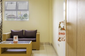 A room with a wicker sofa, a small table, and a wall-mounted sign. - OYO 2947 Cluster Harris Home Stay and Kos (Cimahi)