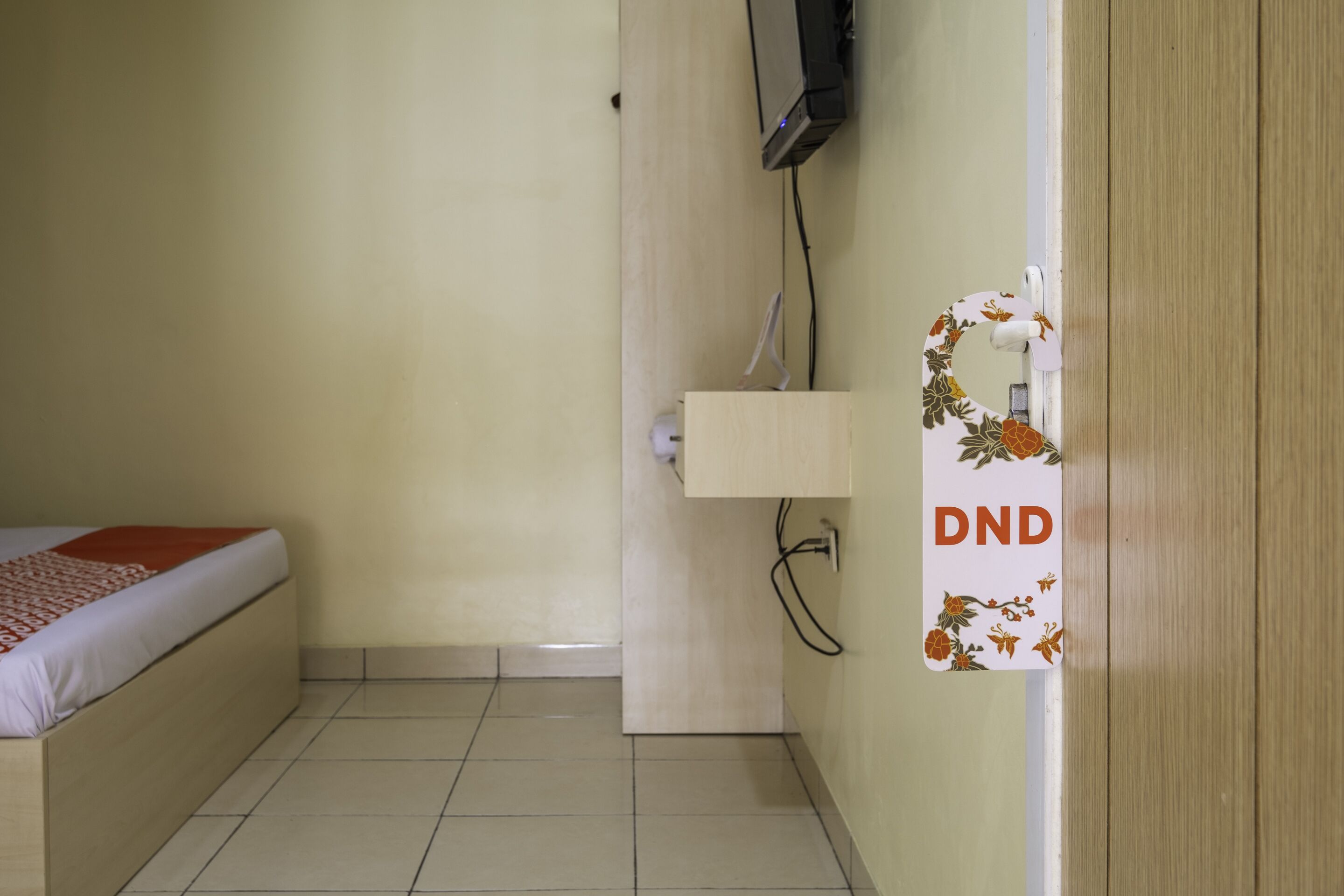 Una habitación con una cama, un armario de madera, un televisor montado en la pared y una puerta con el letrero de no molestar.