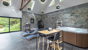 Ein modernes Zimmer mit Steinwand, Whirlpool, Tisch mit Stühlen und Decke mit Holzbalken und Pendelleuchten.