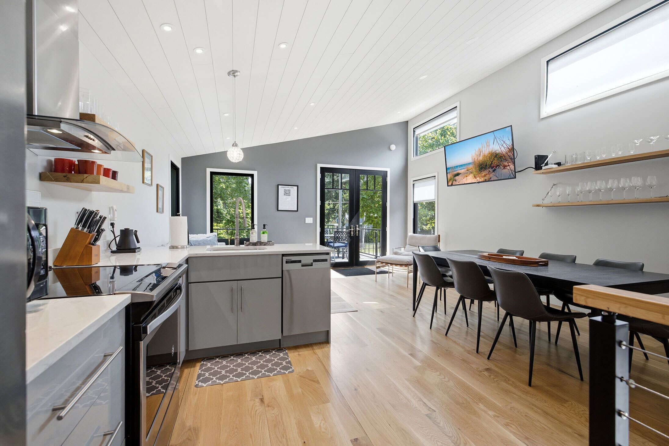 A modern kitchen with a built-in oven, a dining area with a large table and chairs, and a view of the outdoors through the windows.