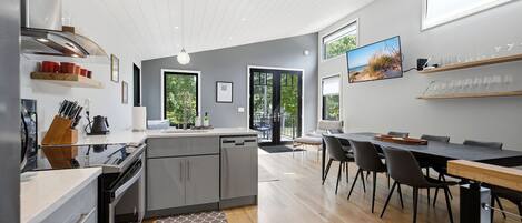 A modern kitchen with a built-in oven, a dining area with a large table and chairs, and a view of the outdoors through the windows.