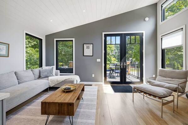 Una sala de estar moderna con un sofá, una mesa de centro y una silla. Hay un ventanal corredero que da a un patio al aire libre.
