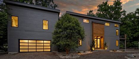 Een modern huis met twee verdiepingen, een garage, grote ramen en een verzorgde tuin.
