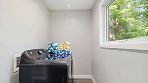 A laundry room with a washing machine, a dryer, and a window with a view of trees.