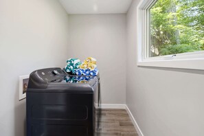 Une buanderie équipée d’un lave-linge, d’un sèche-linge et d’une fenêtre donnant sur les arbres.