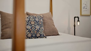 A four-poster bed with a patterned pillow and two plain pillows, a bedside lamp, and a framed picture on the wall.