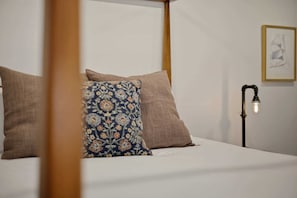 Un lit à baldaquin avec un oreiller à motifs et deux oreillers unis, une lampe de chevet et un tableau encadré au mur.