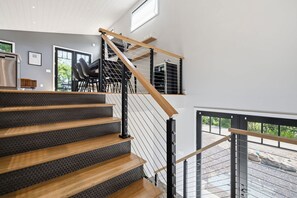 Una escalera moderna con escalones de madera y barandas de metal, que conduce a un nivel superior con vistas al exterior.
