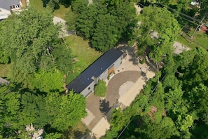 Vista aérea de uma propriedade residencial com uma casa térrea, cercada por vegetação densa e uma entrada pavimentada.