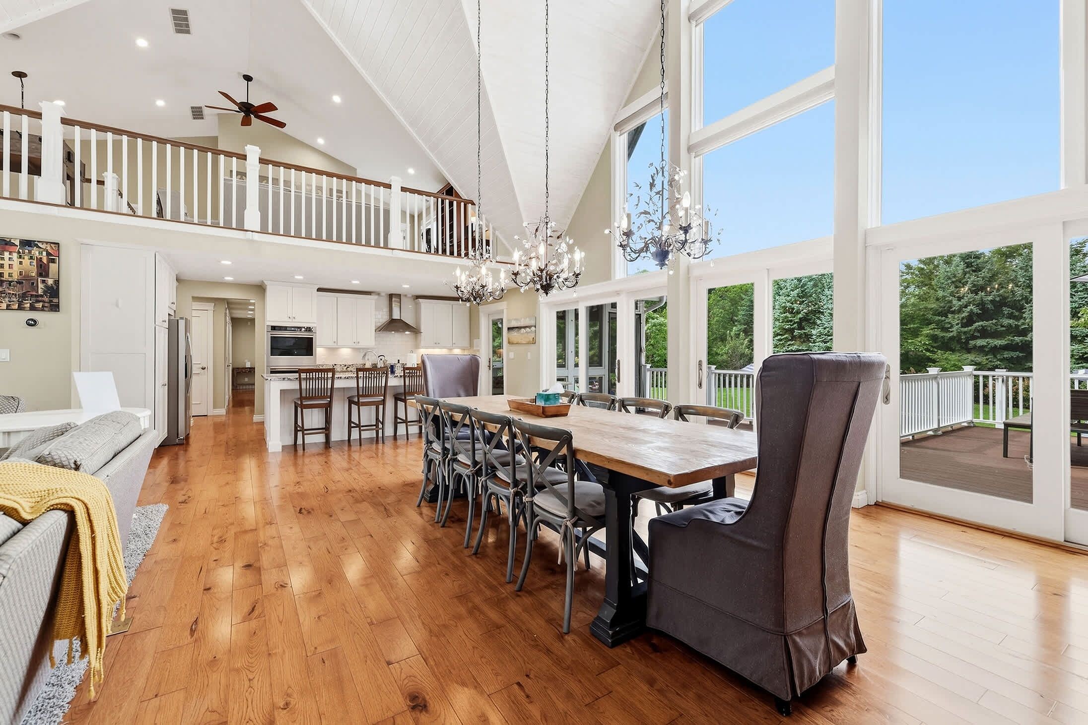A spacious dining area with a high ceiling and large windows, a kitchen with modern appliances, and a cozy seating area with a sofa and a throw blanket.