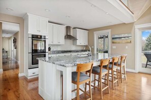 Una cocina con armarios blancos, encimera de mármol y taburetes de madera.