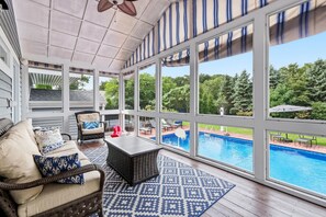 A covered patio with a view of a swimming pool, wicker furniture, and a patterned rug. - Juniper Presents Main Destination: Pet-Friendly, Hot Tub, Pool & Firepit (Grand Beach)