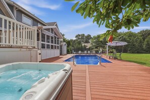 A swimming pool with a hot tub, a covered deck, and a view of a house with a balcony.