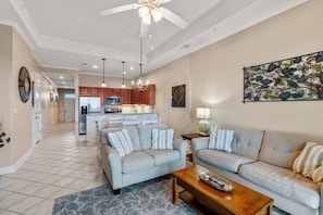 A spacious living area with a sofa, coffee table, and a dining area with a kitchen in the background.