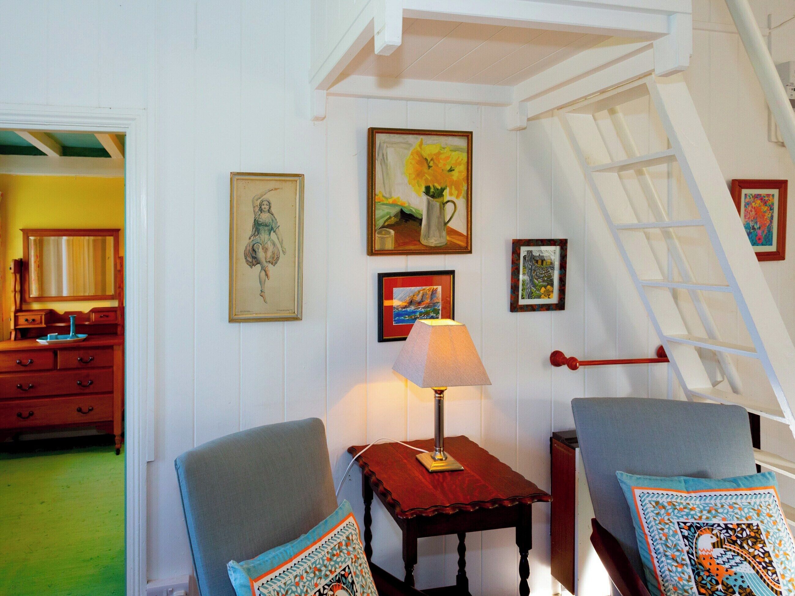 A room with a wooden dresser, a table with a lamp, and a chair with a patterned cushion.