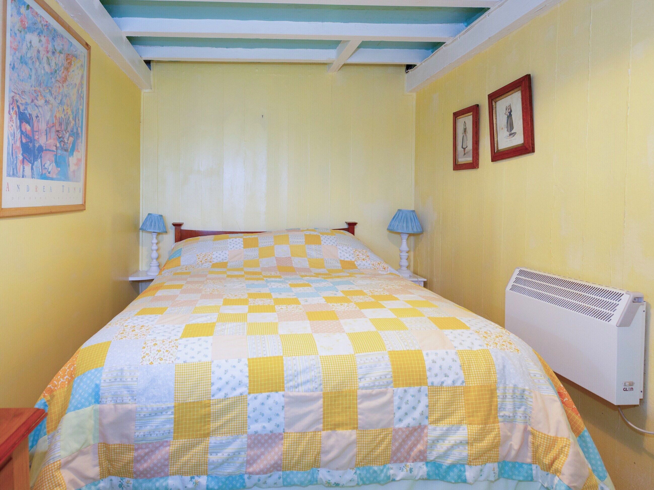 A room with a bed, two bedside lamps, a wall-mounted air conditioner, and two framed pictures.