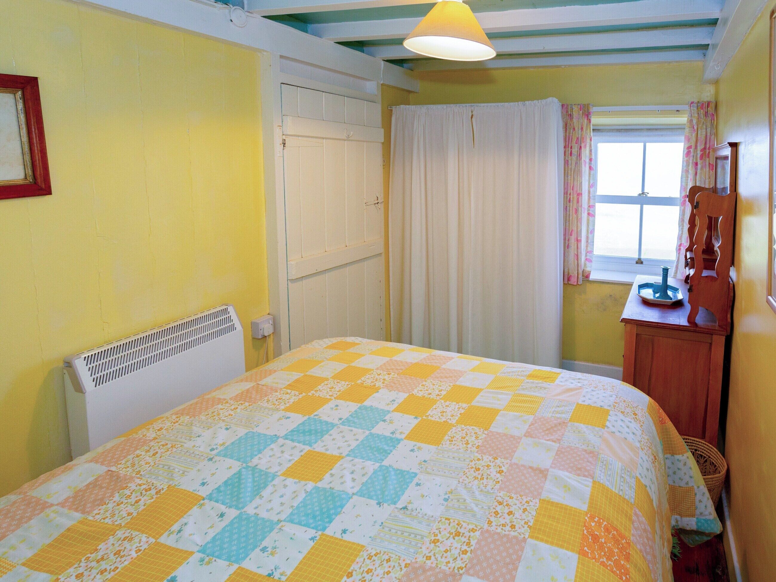 A room with a bed covered in a checkered quilt, a radiator, a window with curtains, and a wooden dresser.