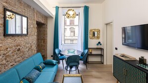 A modern living room with a stone wall, a blue sofa, a dining table with chairs, and a TV on the wall. - Solferino apartment near Roma Termini central station (Rome)