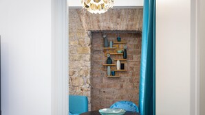 A room with a brick wall, a wooden shelf with decorative items, a round table with a bowl, and blue chairs. - Solferino apartment near Roma Termini central station (Rome)