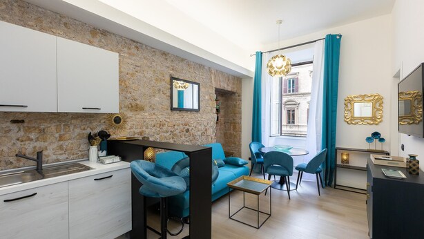 A modern apartment with a kitchen, dining area, and living room. It features a stone wall, a blue sofa, and a dining table with chairs. - Solferino apartment near Roma Termini central station (Rome)