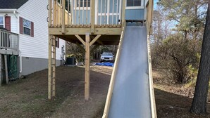 A wooden slide structure with a platform and a ramp leading to a house.