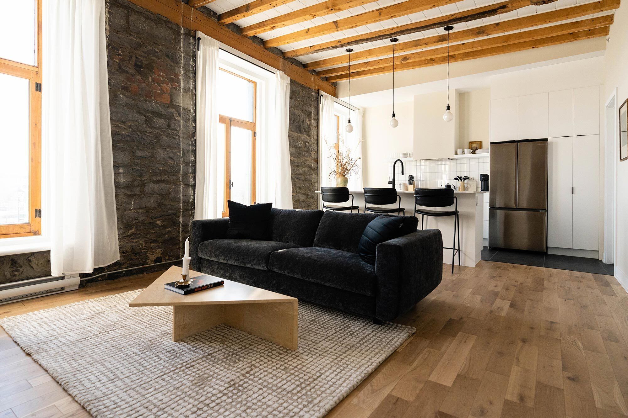 A modern living room with a dark sofa, a coffee table, and a kitchen in the background.