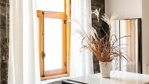 A kitchen with a wooden ceiling, white curtains, a large window, a stainless steel refrigerator, and a white vase with dried plants on the counter. -  Maison Place Royale by Luxury In Transit (Montreal)