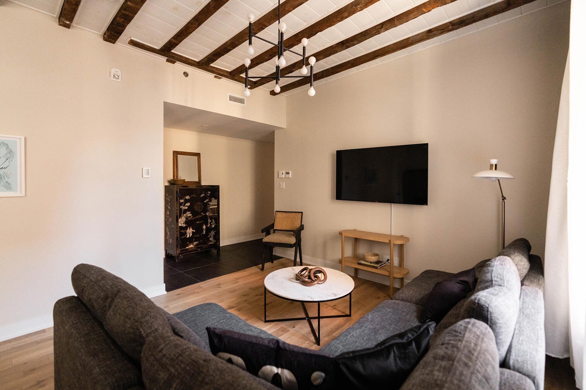 Una sala de estar moderna con un sofá seccional, una mesa redonda de centro, un televisor montado en la pared y un mueble de madera.