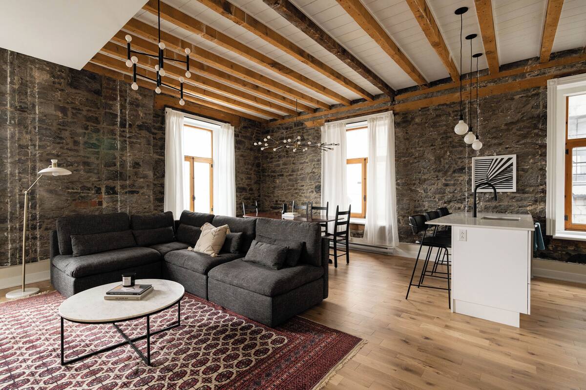 A modern living room with a sectional sofa, a small coffee table, and a kitchen area with a white countertop and bar stools.
