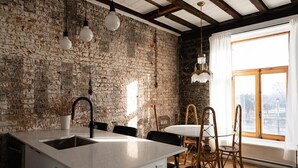 A kitchen with a rustic brick wall, a white island with a sink, and a dining area with wicker chairs. -  Maison Place Royale by Luxury In Transit (Montreal)